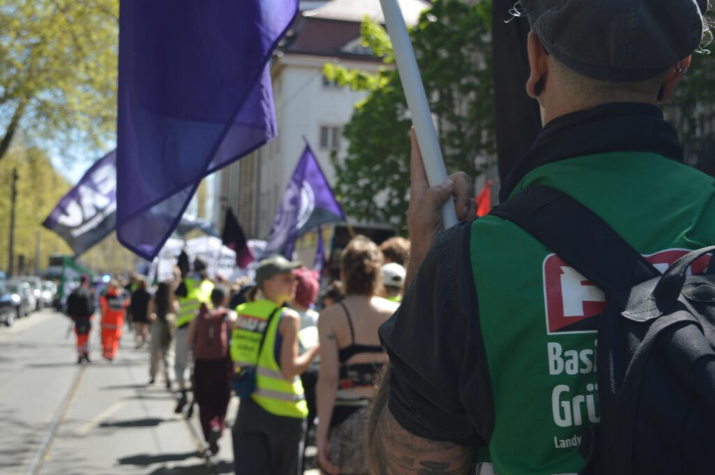 Ein Demonstrationszug von hinten seitlich fotografiert mit zahlreichen Fahnen und verschieden farbigen FAU-Westen.