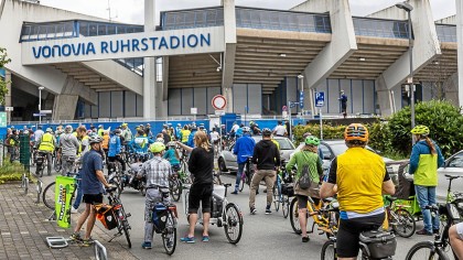Eine Gruppe von Radfahrern steht vor dem Vonovia Ruhrstadion.