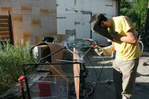 Ein Foto mit einem Mann, der ein Lastenrad zusammen schweißt.