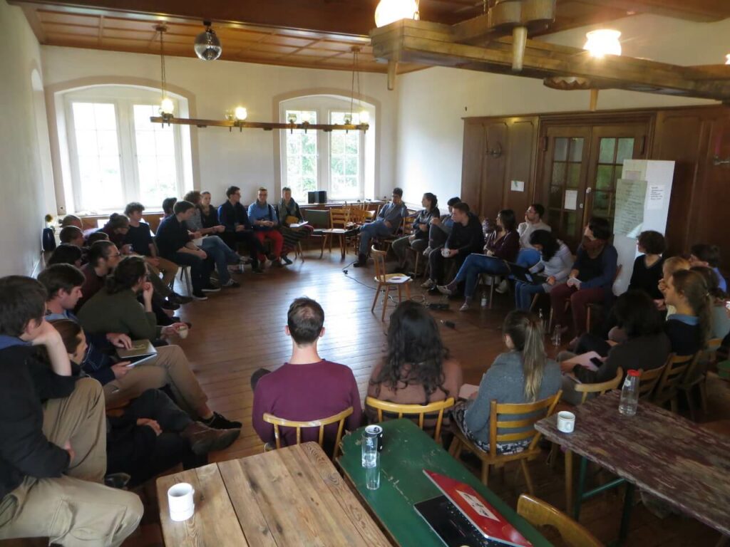Studierende der Hochschule für Gesellschaftsgestaltung in einer Diskussionsrunde. In einem schönem Raum mit Holzboden und -decke.