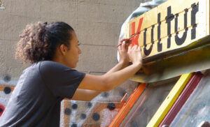 Das Foto einer Frau, die das Wort: Kultur auf Holzleisten malt